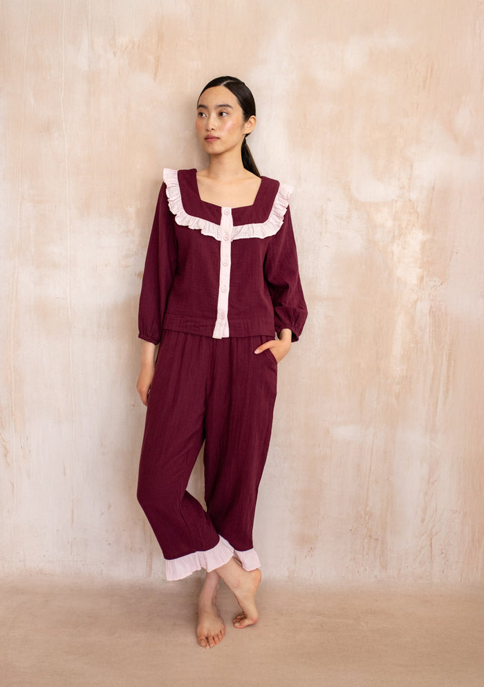 Burgundy pyjama set with soft pink trim, featuring a button-up top with ruffled neckline and matching trousers with ruffle hem.
