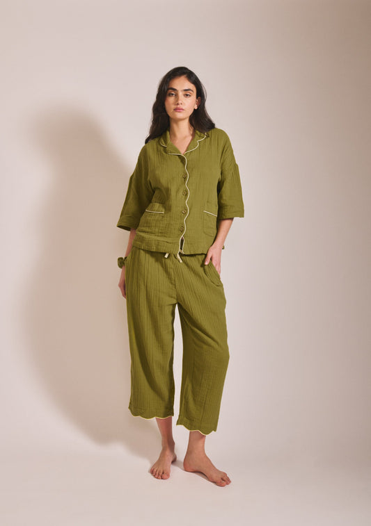Model wearing a relaxed moss green pyjama set with short sleeves, button front, contrast piping detail, and loose cropped trousers.