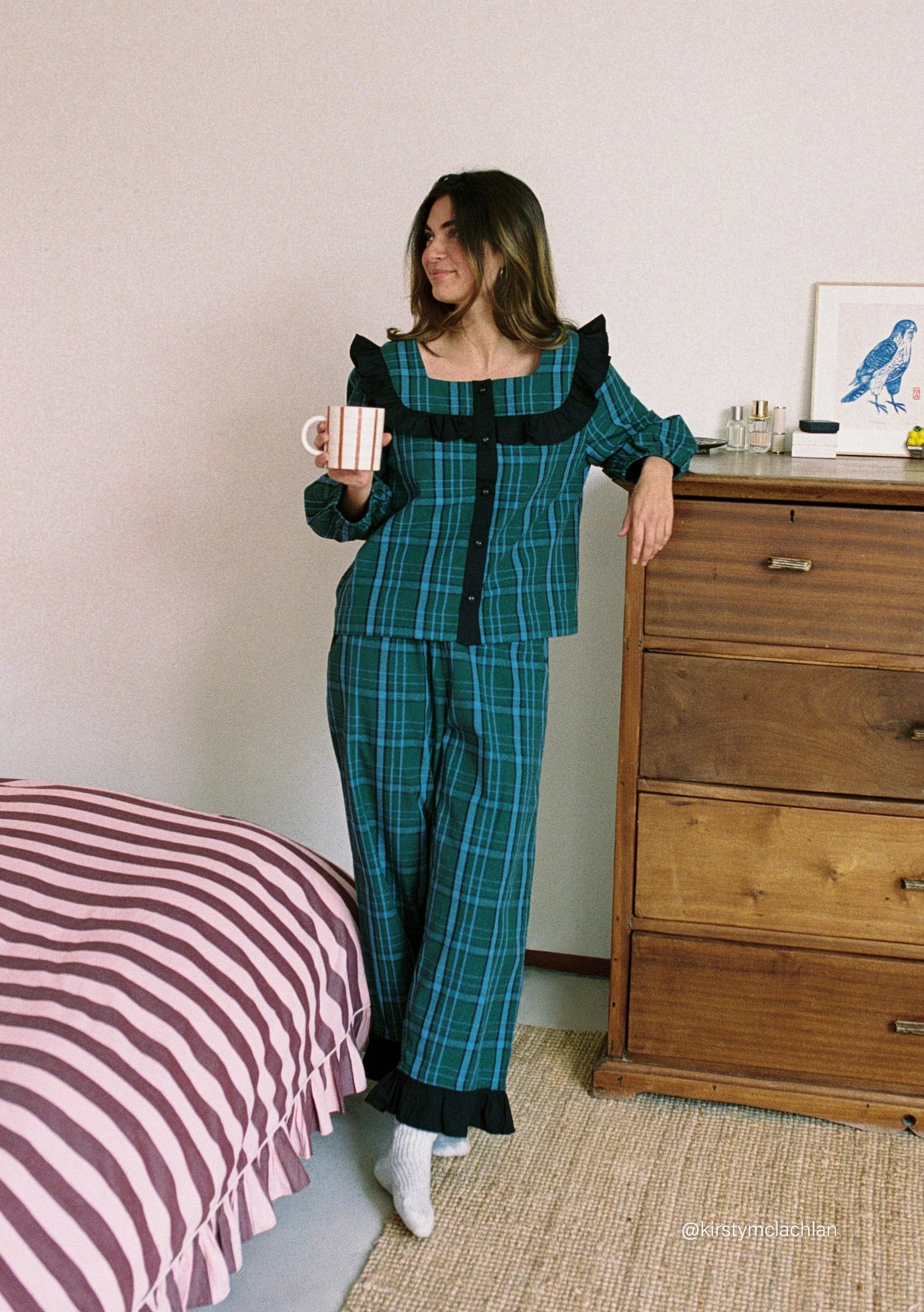 Woman in a teal plaid outfit holding a mug in a bedroom. Pyjamas are by TBCo and are filtered by Shop My Palette for the Deep Winter, Cool Winter, and Clear Winter colour seasons.