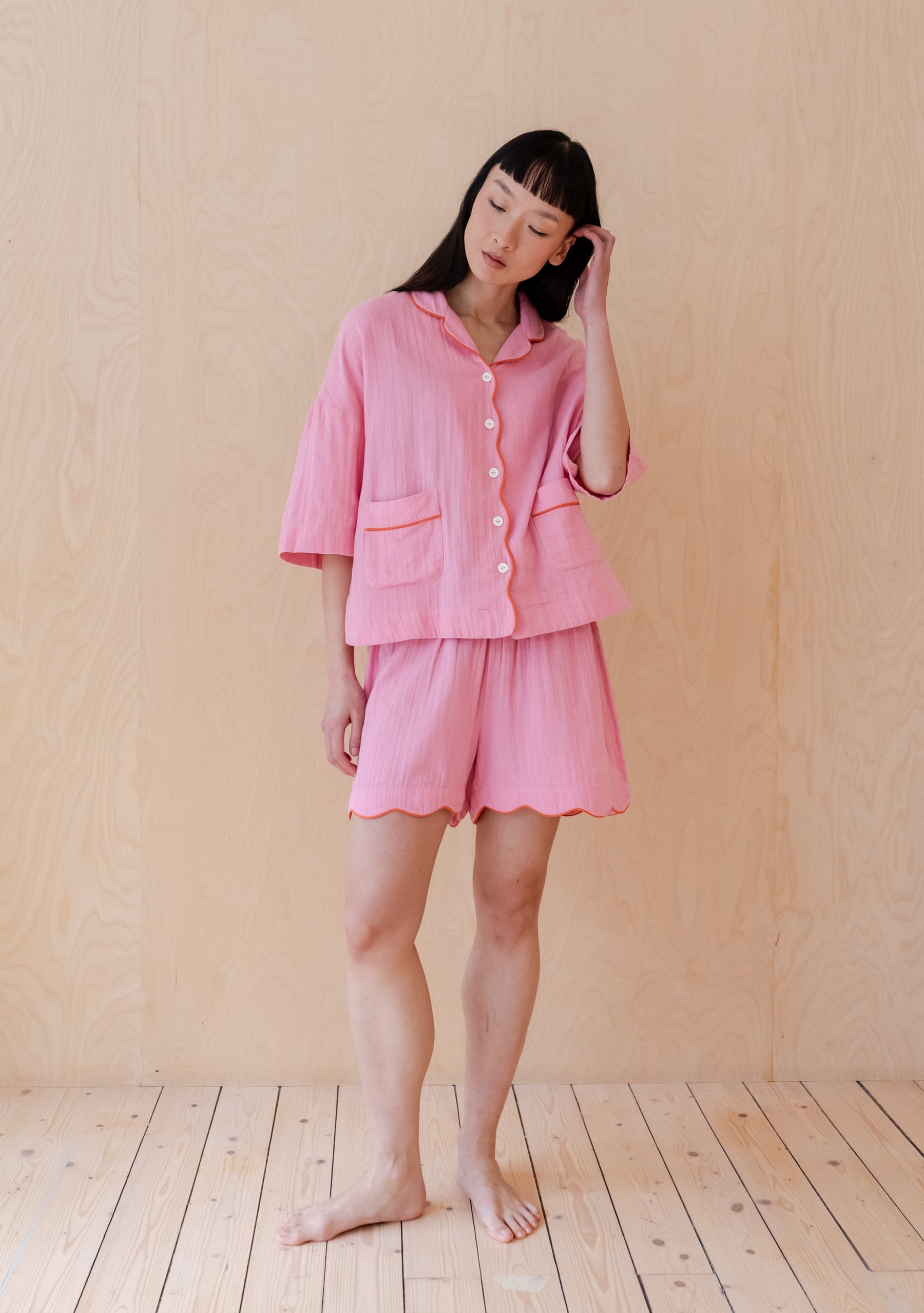 Relaxed pink short pyjama set with short sleeves, button front, contrast piping, and scalloped hem shorts.
