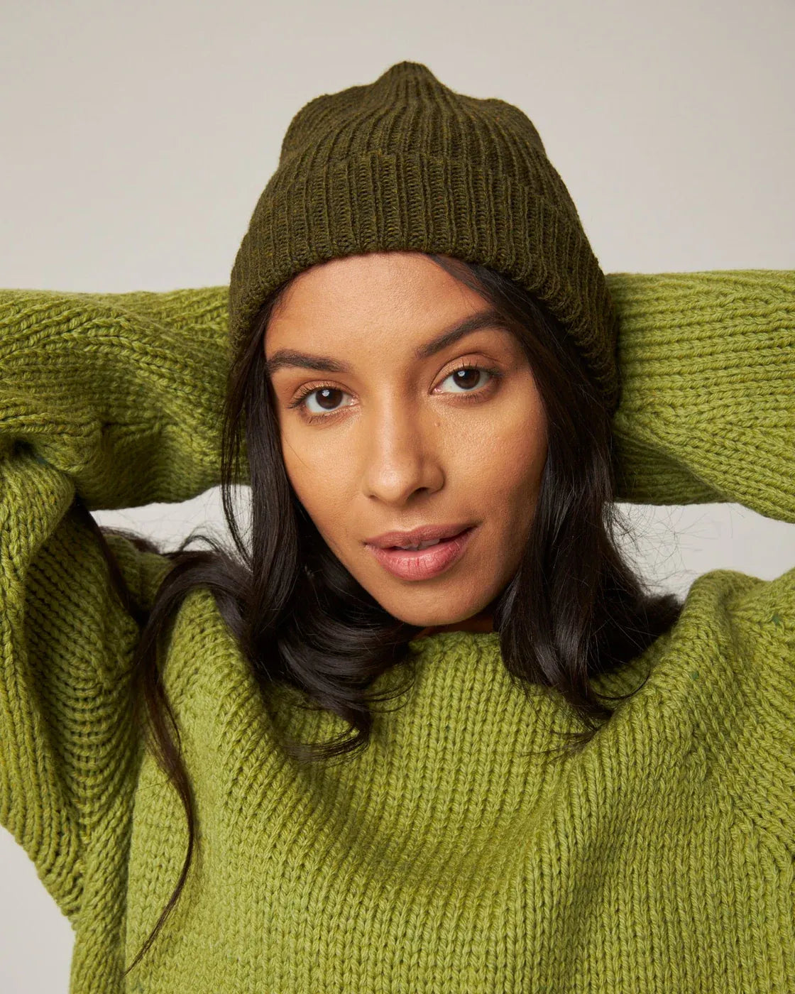 Woman wearing a green knit sweater and beanie against a neutral background. Knitwear is from Peregrine Clothing and filtered on Shop My Palette for the Warm Spring, Warm Autumn and Deep Autumn colour seasons.