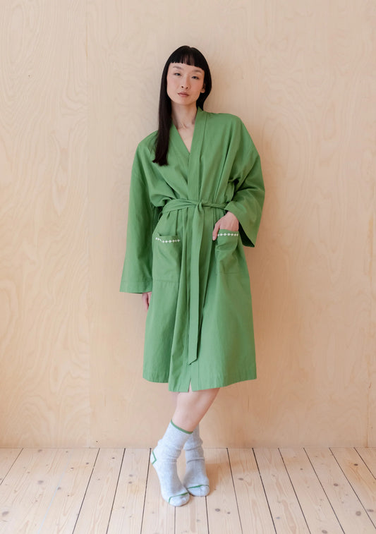 Model wearing a grass green cotton robe, leaning against a wooden wall. Robe is by TBCo and is filtered for the Clear Spring, Light Spring, and Warm Spring colour seasons by Shop My Palette.