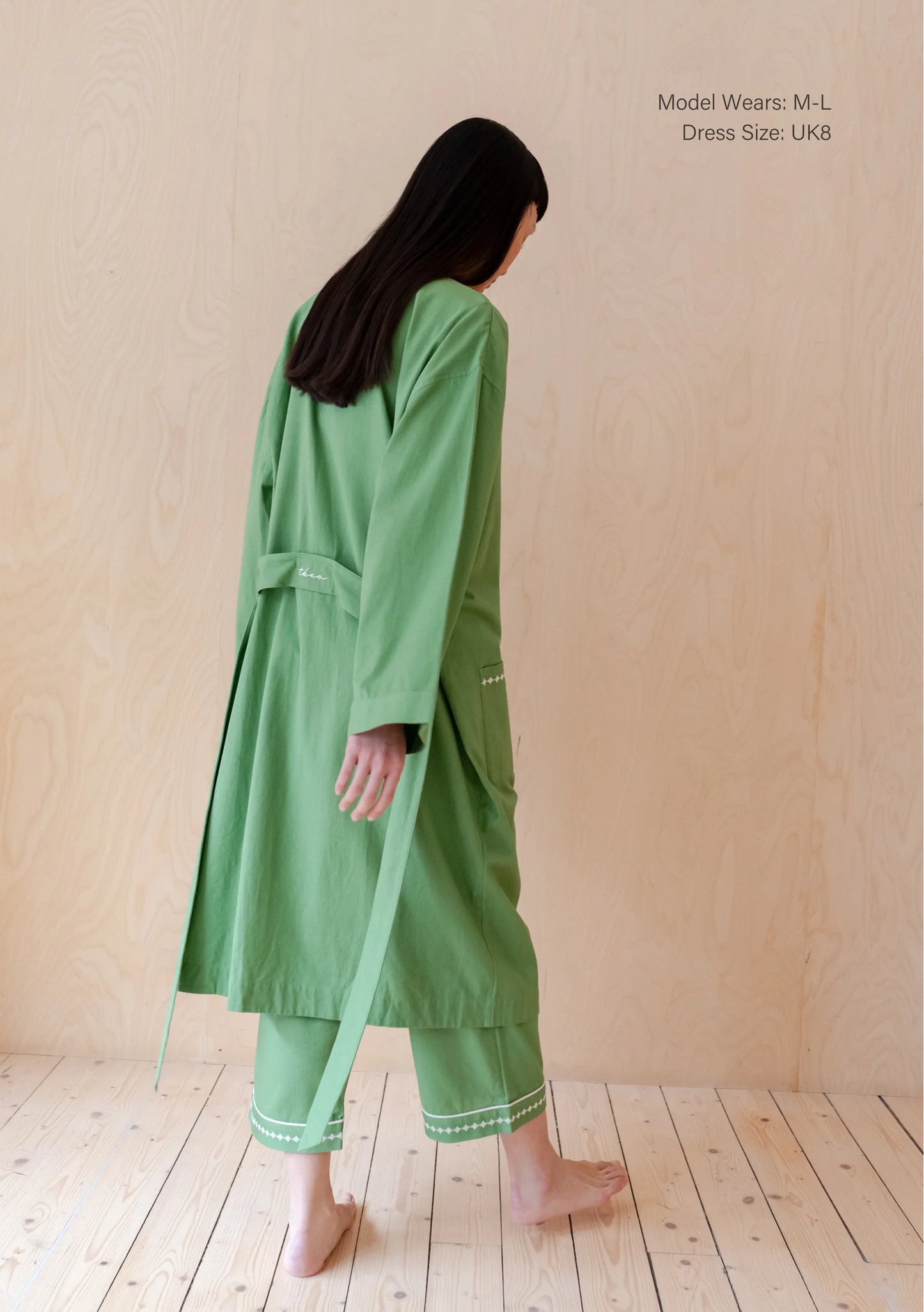 Person wearing a grass green cotton robe, standing in a room with wooden flooring and beige walls. Robe is by TBCo and is filtered for the Clear Spring, Light Spring, and Warm Spring colour seasons by Shop My Palette.