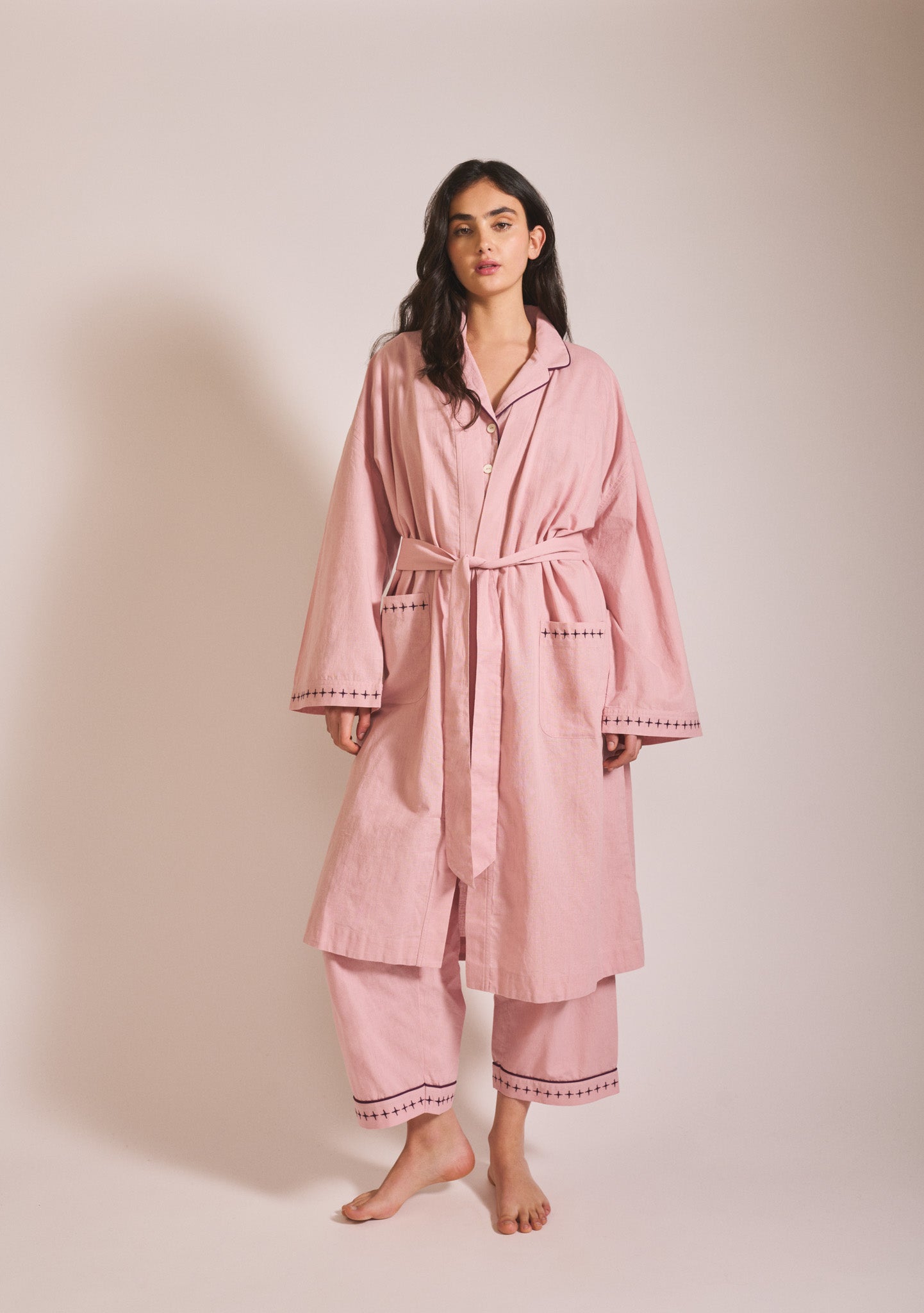 Model wearing a relaxed dusty pink robe layered over matching pyjama bottoms, with long sleeves, tie waist, and loose cropped trousers.
