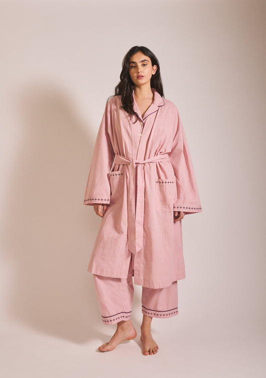 Model wearing a relaxed dusty pink robe layered over matching pyjama bottoms, with long sleeves, tie waist, and loose cropped trousers.