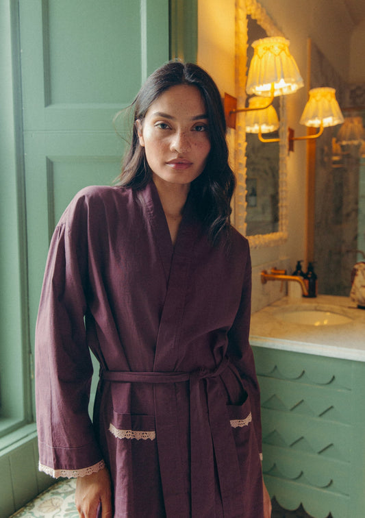 Model wearing a soft plum cotton robe with lace trim, standing in a bathroom with green wooden walls.
