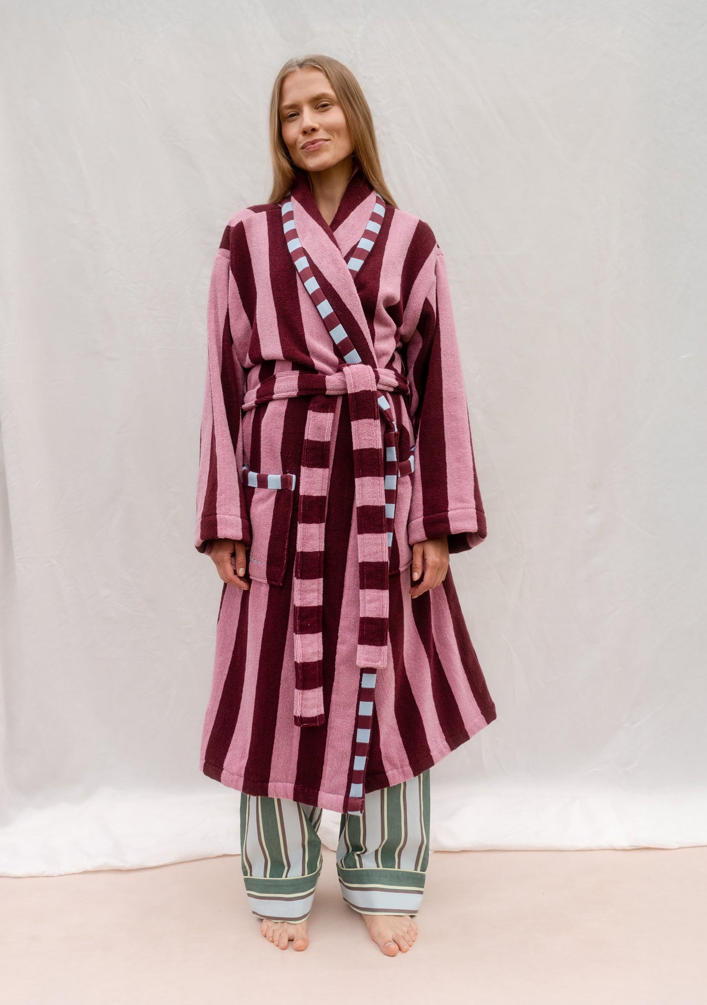 Pink and burgundy striped robe with belt, featuring alternating dusty rose and deep berry vertical stripes, worn over striped trousers.