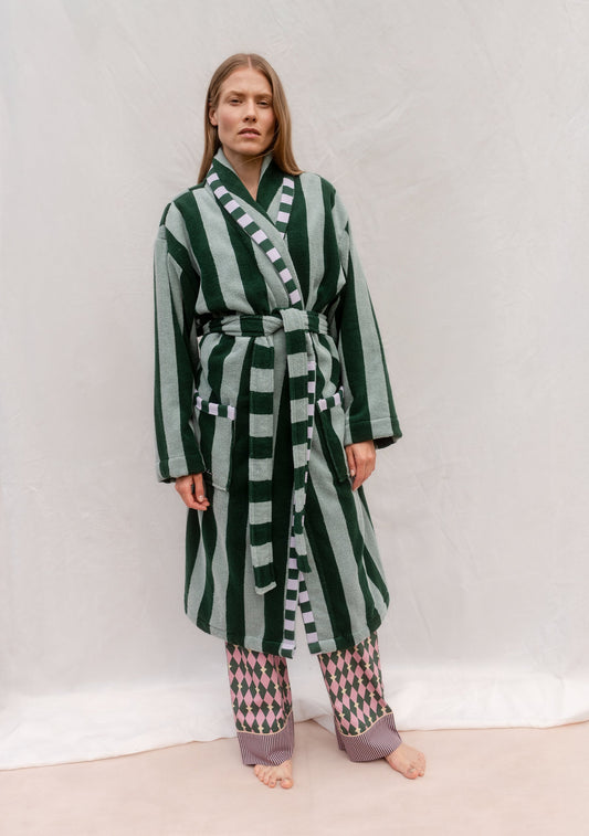 Green terry cotton towelling striped robe with belt, featuring alternating dark forest green and soft sage vertical stripes, worn over patterned trousers.