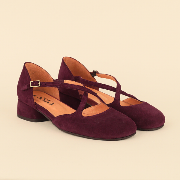 A pair of women's low block-heel Mary Jane shoes in deep burgundy suede, featuring crisscross ankle straps with gold-tone buckles and a tan insole, shown on a solid light beige background.
