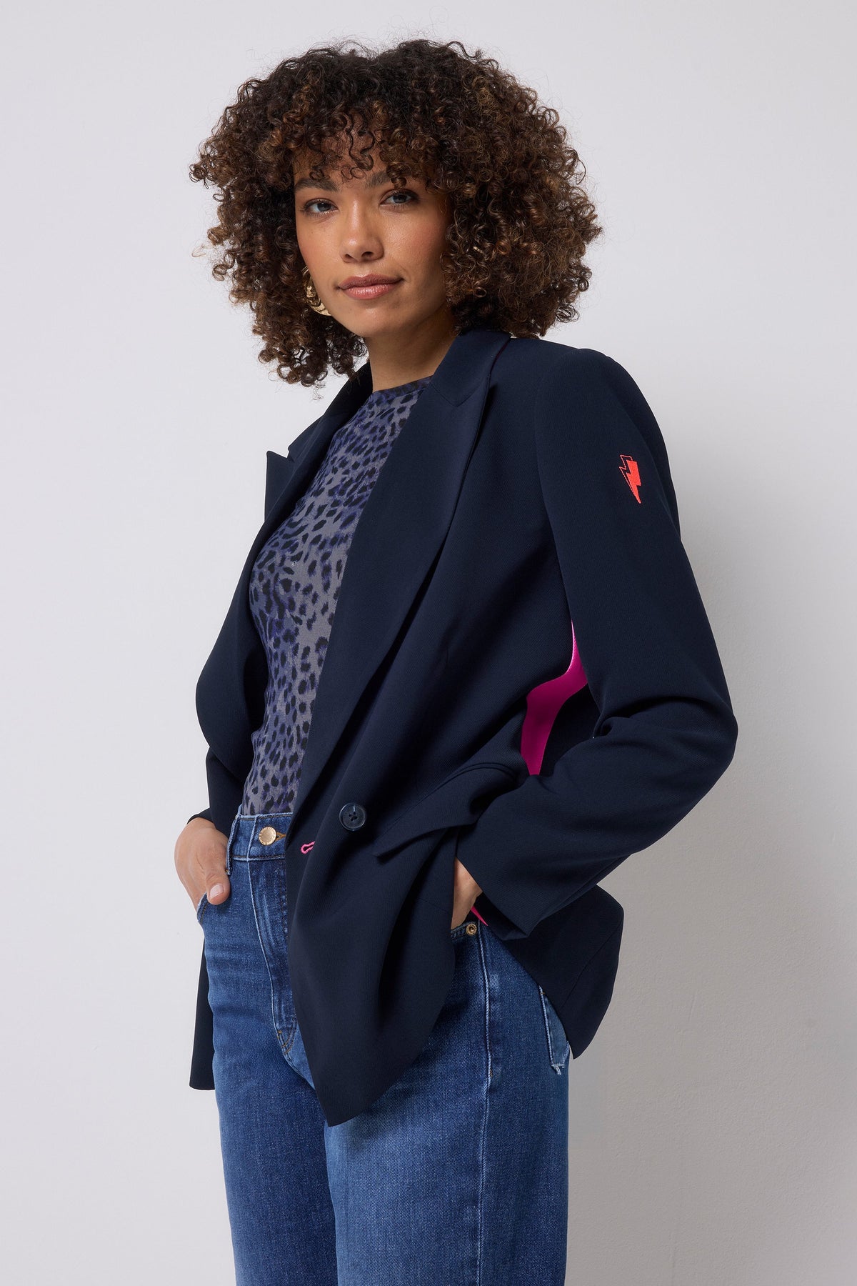 Model wears navy blazer with pink stripe over a leopard-print top and blue jeans.