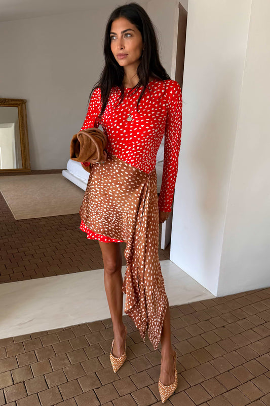 A woman models a red and white polka dot long-sleeve top paired with a brown and white polka dot wrap skirt, holding a brown clutch, in an indoor setting with a tiled floor.