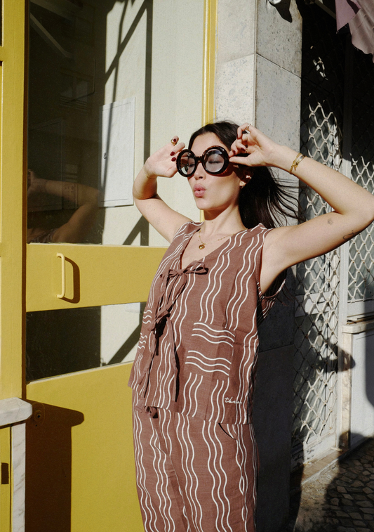 Sleeveless brown top with cream wavy stripe pattern and tie-front fastening, worn with matching trousers and oversized sunglasses