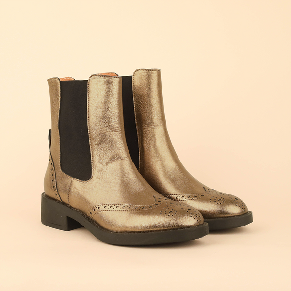 A pair of metallic gold leather Chelsea boots with black elastic side panels and black soles, photographed on a solid light beige background.