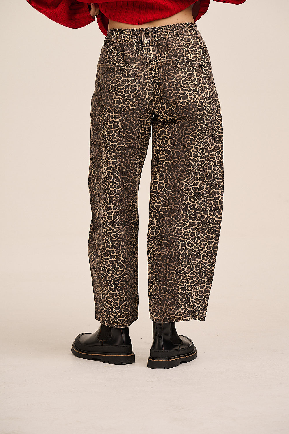 A person shown from the waist down wearing leopard-print wide-leg pants, a red cropped sweater, and black boots against a plain light beige studio background.