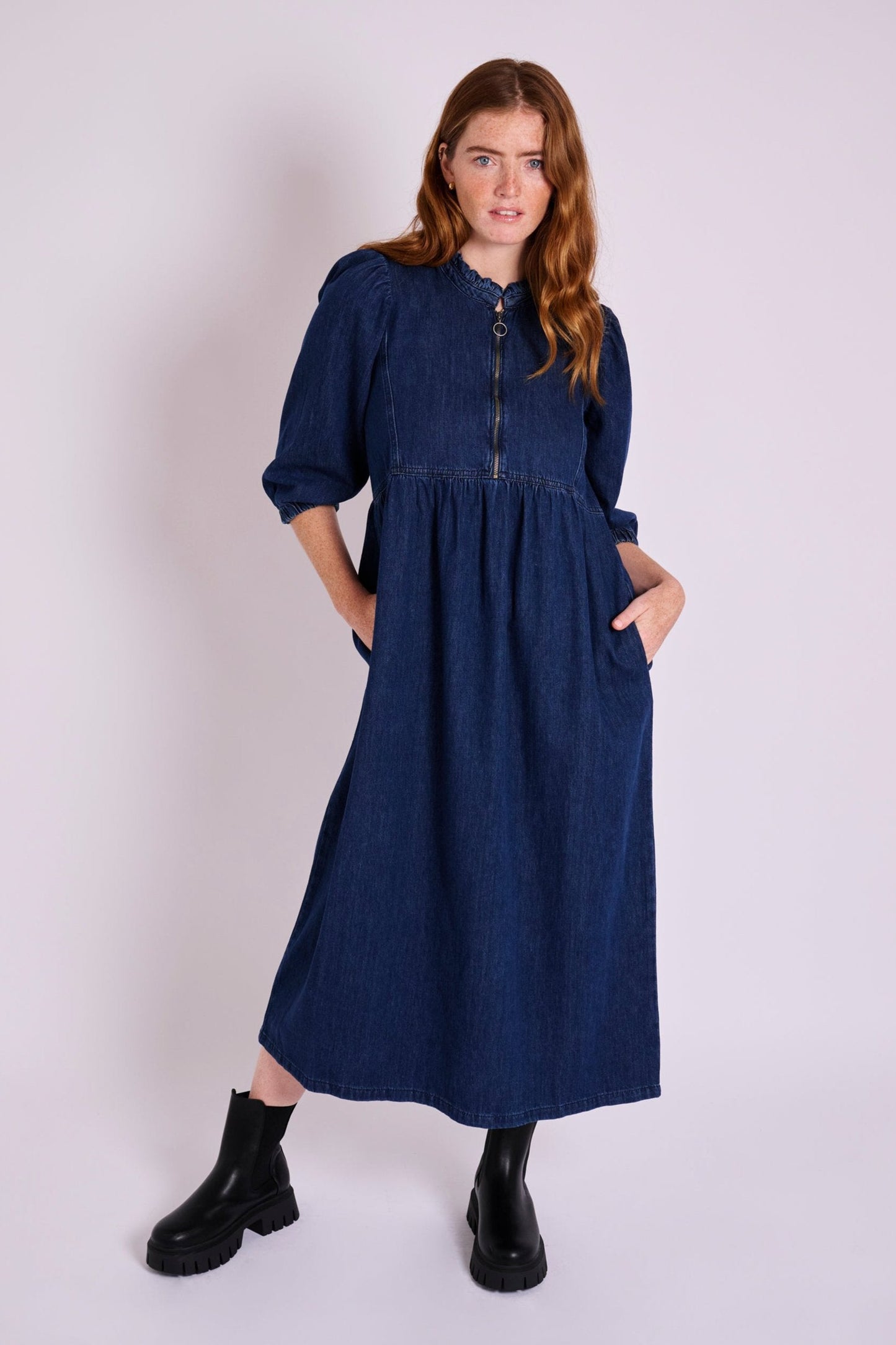 Dark blue denim midi dress with three-quarter sleeves, front zip detail, gathered waist, and side pockets.