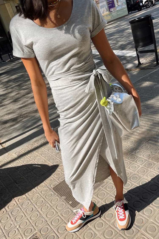 Light grey short sleeve midi dress with wrap tie detail, ruched draping, and fitted silhouette