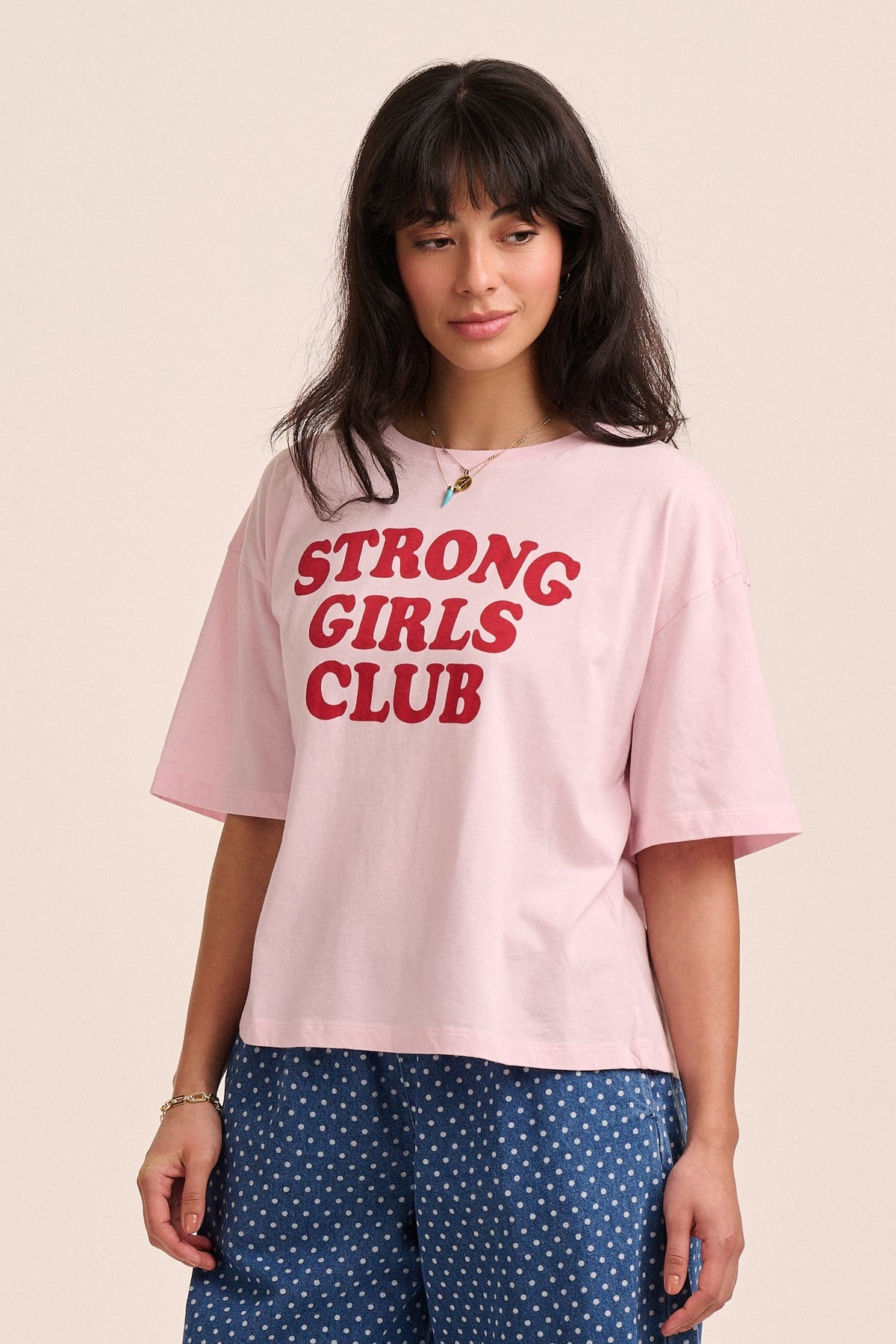 Woman wearing a pink t-shirt with 'STRONG GIRLS CLUB' text on a beige background