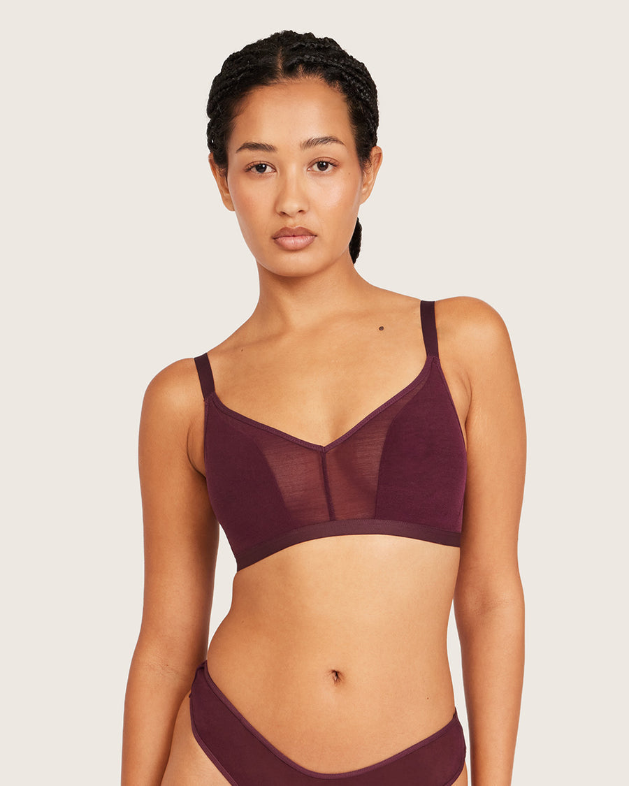 A woman modeling a matching burgundy mesh and solid underwire bra and high-waisted briefs against a light beige studio background.