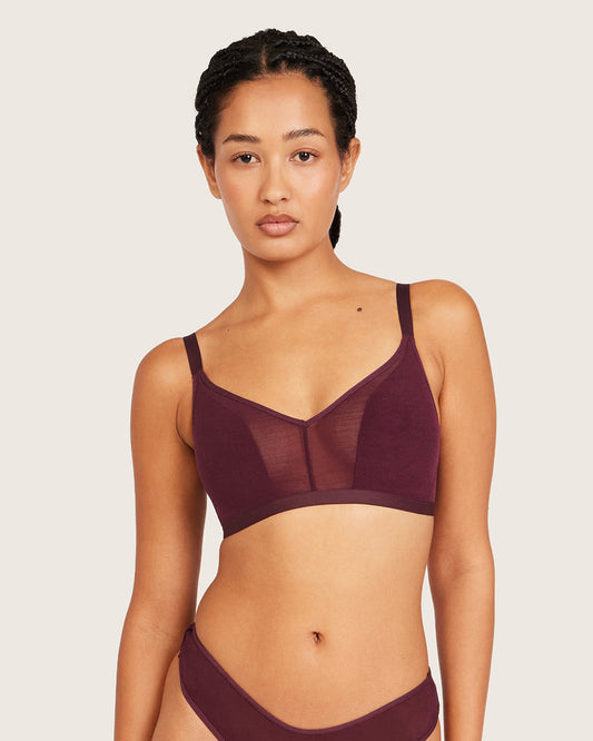 A woman modeling a matching burgundy mesh and solid underwire bra and high-waisted briefs against a light beige studio background.