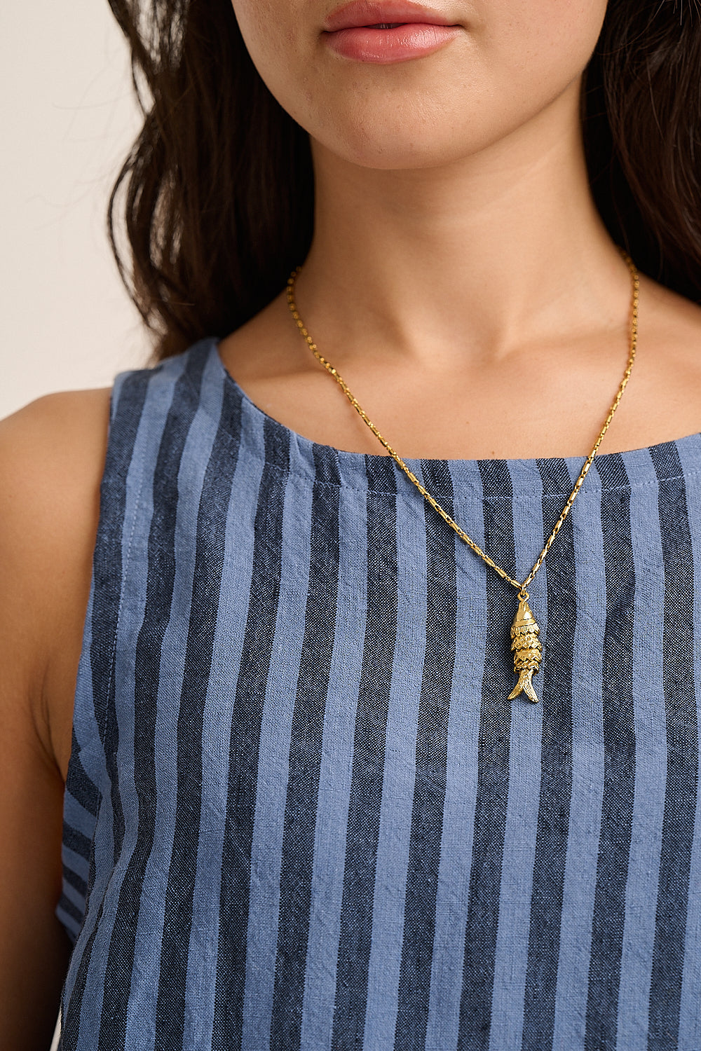 Model wears gold fish pendant necklace over a blue striped denim top.