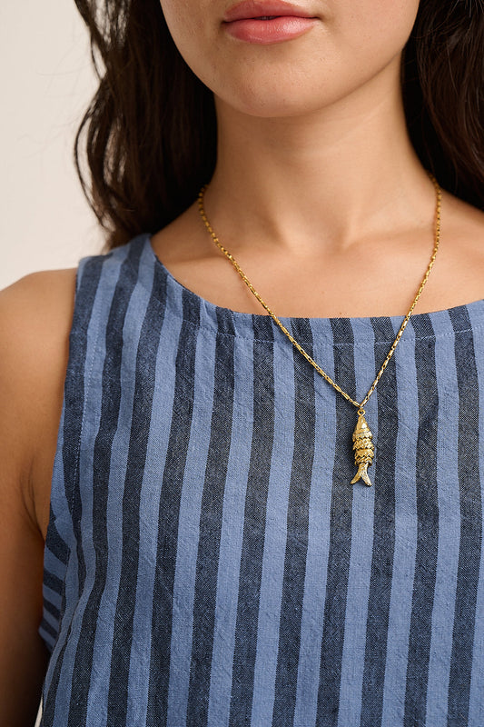 Model wears gold fish pendant necklace over a blue striped denim top.